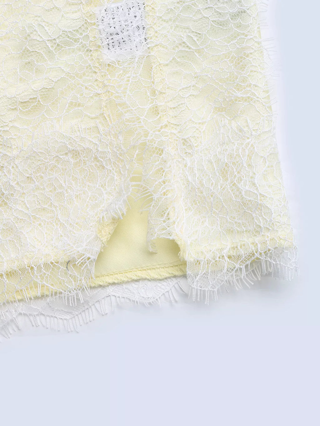 Close-up of the white eyelash lace draped over a fold of pastel yellow satin, showing the frilled lace edge and the satin sheen.