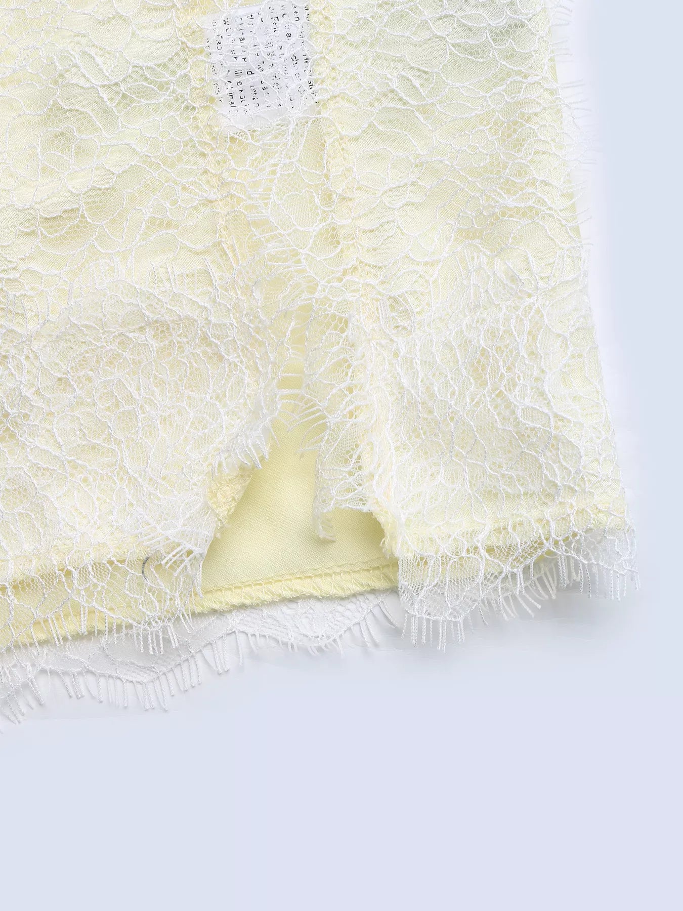 Close-up of the white eyelash lace draped over a fold of pastel yellow satin, showing the frilled lace edge and the satin sheen.
