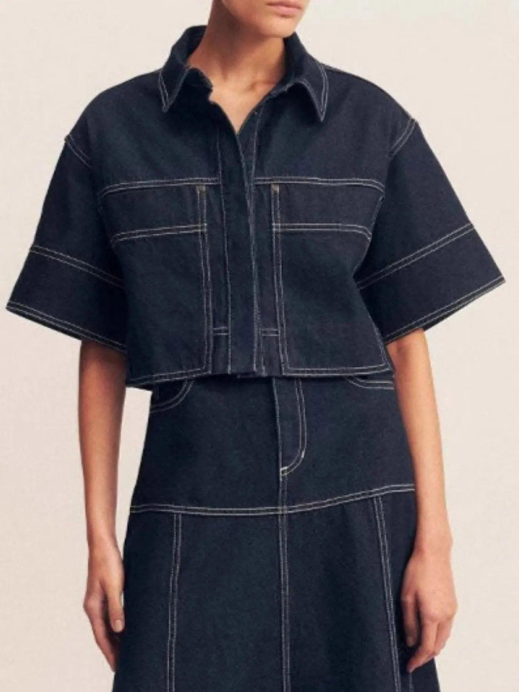 Midnight blue cropped short-sleeve contrast-stitch denim top, front view showing the pointed collar, button placket, chest patch pockets, and boxy cropped fit with bold white contrast stitching.
