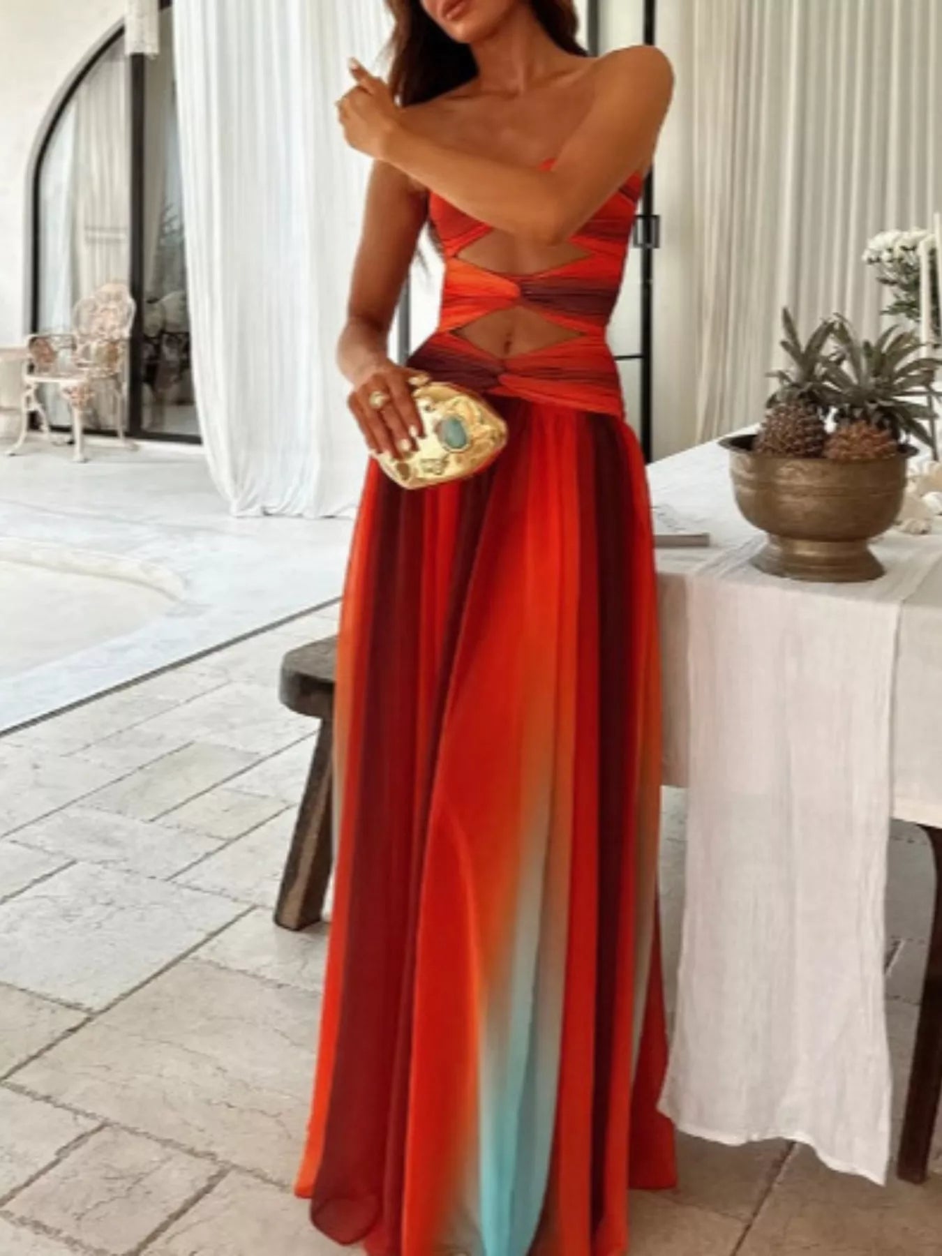 Orange Strapless Twisted Cutout Maxi Dress, mid-body view showing the twisted bust panels, peekaboo waist cutout, and the multi-tonal sheer skirt against an indoor backdrop.
