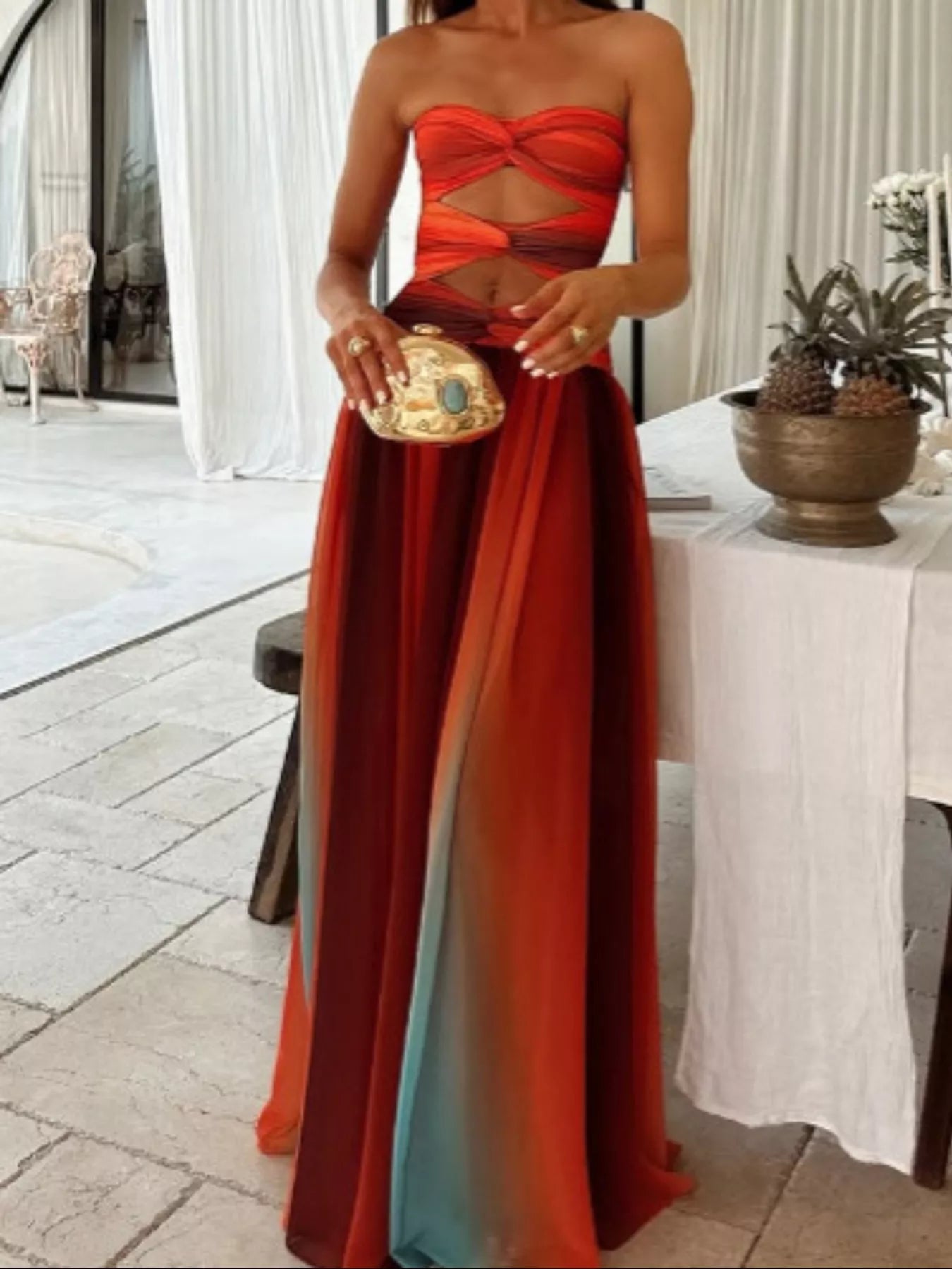 Orange Strapless Twisted Cutout Maxi Dress, full-body front view showing the gathered strapless bust, twisted center panels, peekaboo waist cutout, and sheer flowing skirt in tonal orange, coral, and dusty teal.