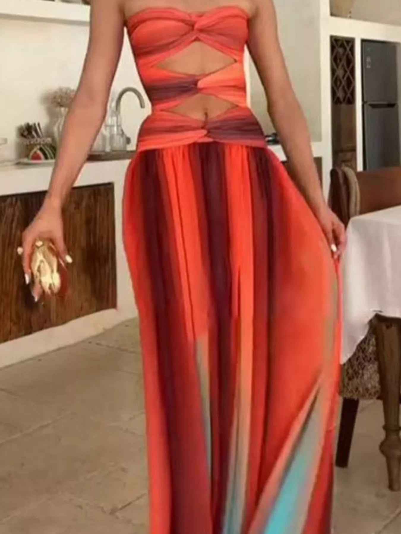 Orange Strapless Twisted Cutout Maxi Dress styled with a beaded clutch and gold rings, showing the twisted bust, waist cutout, and floor-length sheer chiffon skirt.
