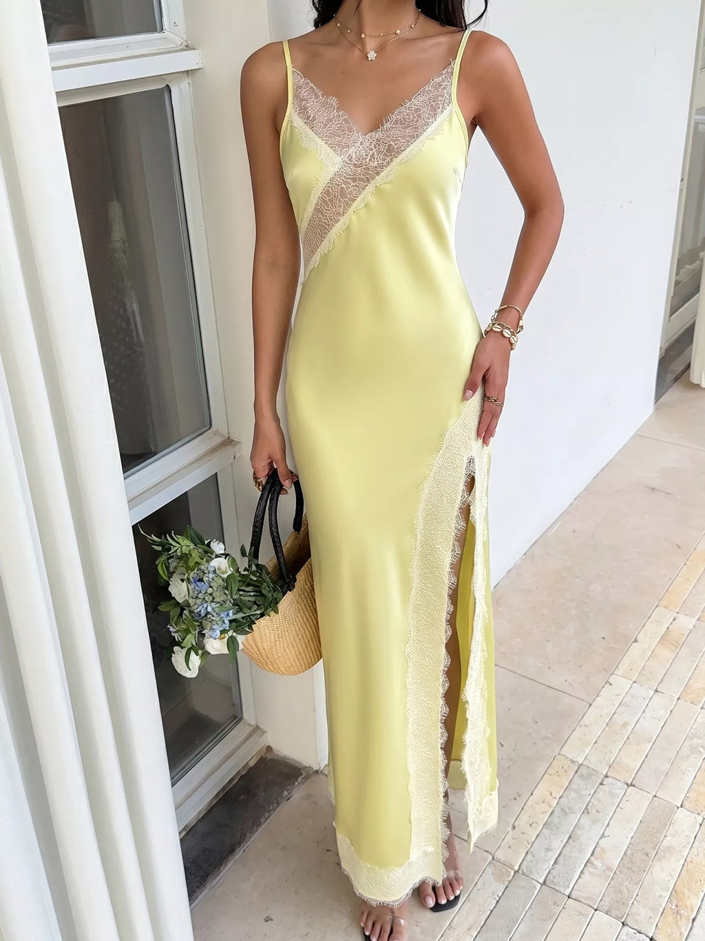 Full-length front view of the Pastel Yellow Lace-Trim Slip Midi Dress in a white French-door doorway, styled with a straw basket bag of white and blue flowers.