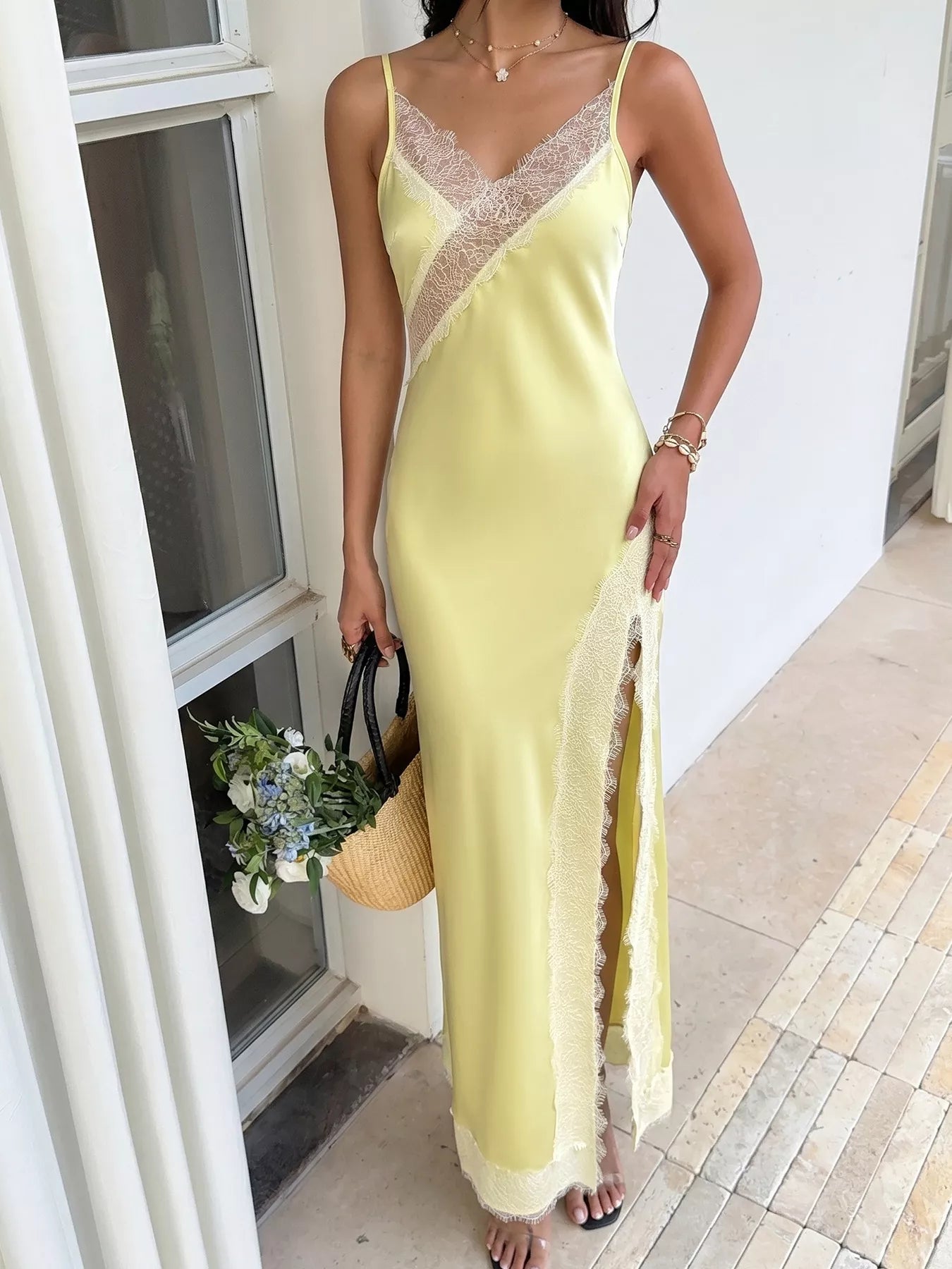 Full-length front view of the Pastel Yellow Lace-Trim Slip Midi Dress in a white French-door doorway, styled with a straw basket bag of white and blue flowers.
