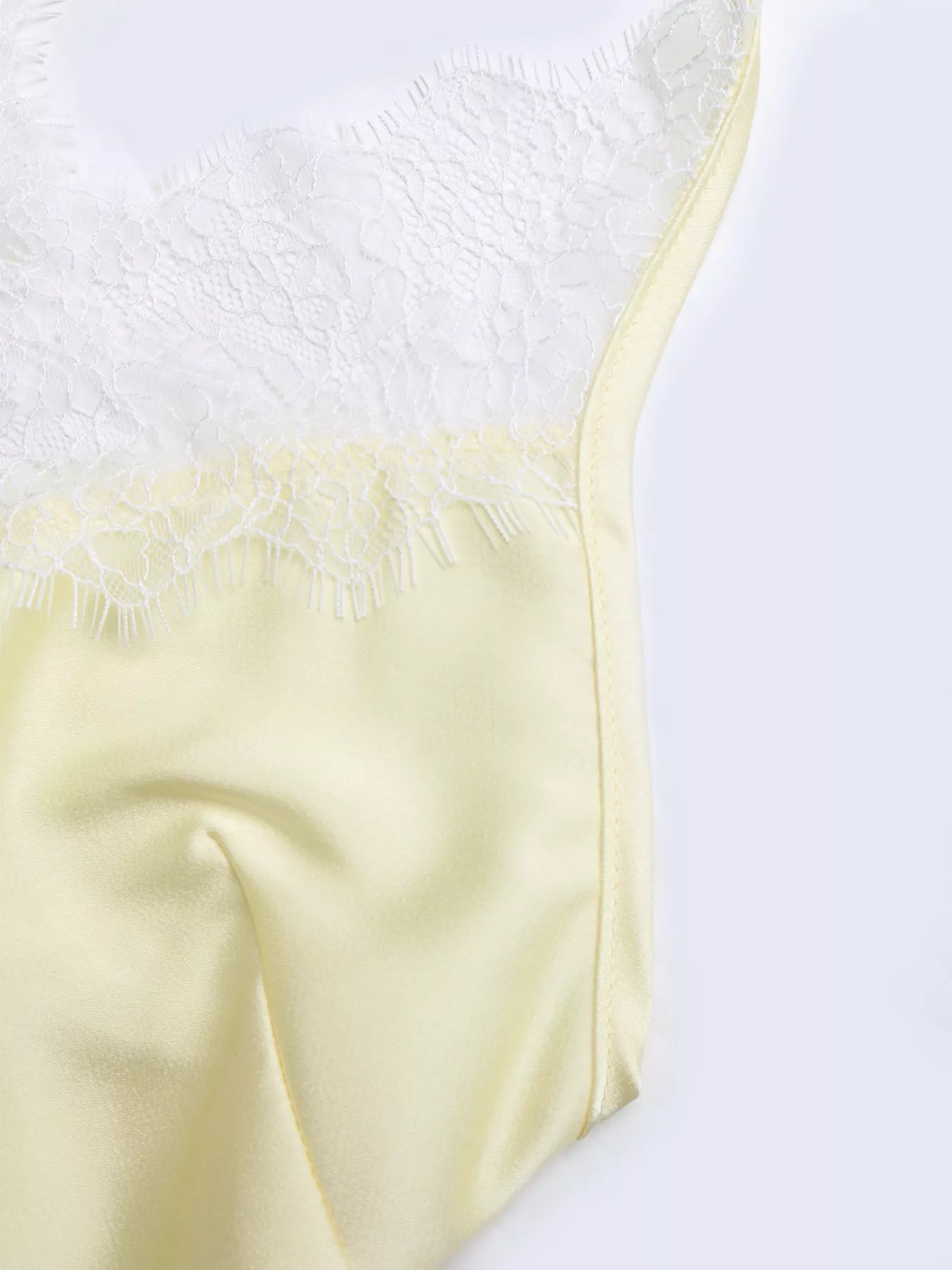 Close-up detail of the Pastel Yellow Lace-Trim Slip Midi Dress, showing the white eyelash lace stitched to the pastel yellow satin.