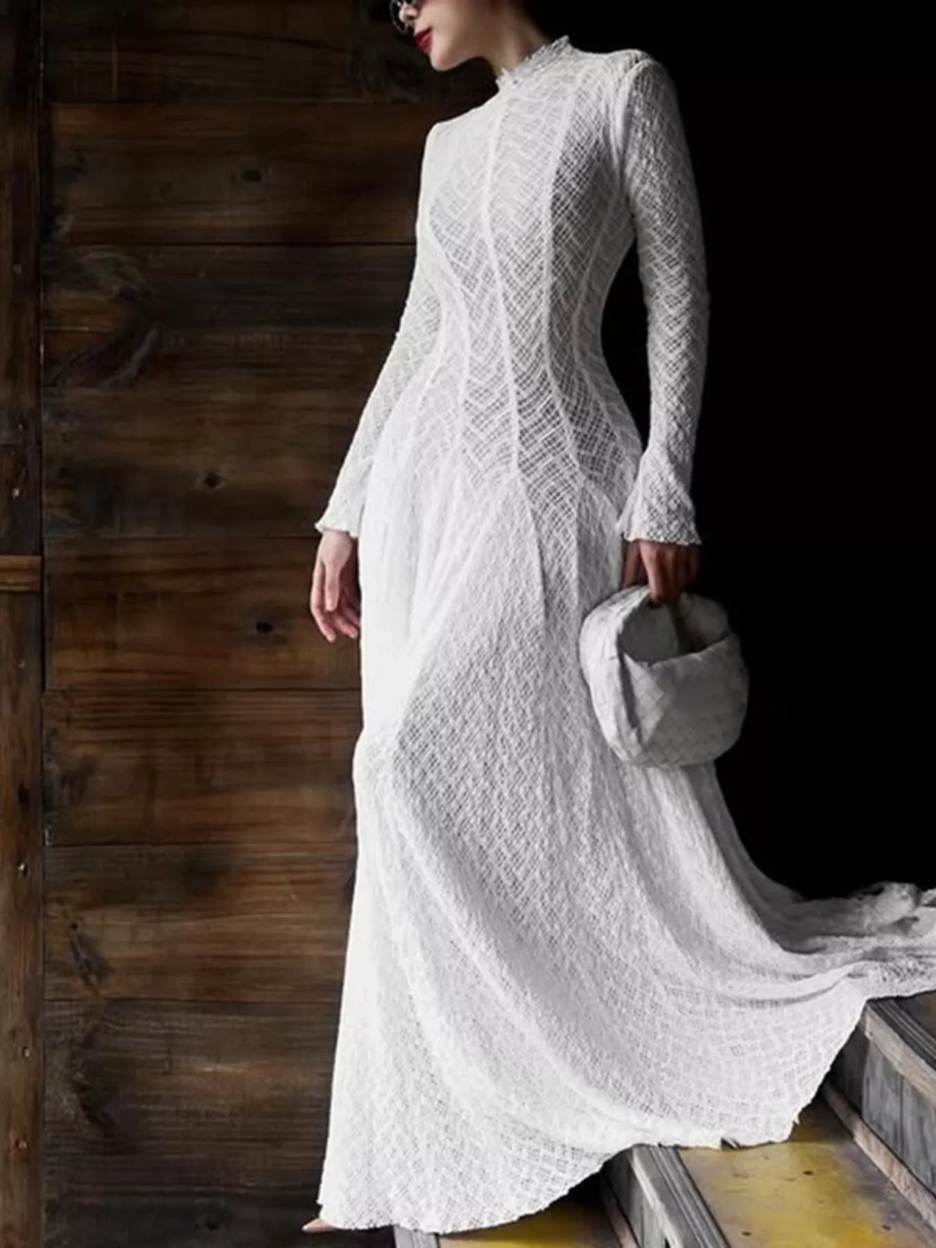 White textured lace mock-neck long-sleeve maxi dress, full-length front view against dark wood doors, styled with a quilted gray top-handle bag.